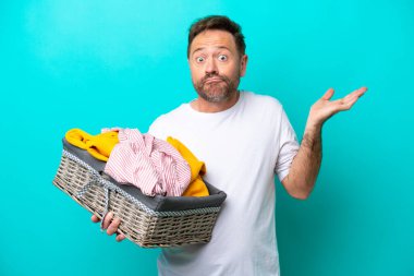 Mavi arka planda soyutlanmış çamaşır sepetini tutan orta yaşlı bir kadın el kaldırırken şüpheye düşüyor.