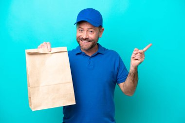 Orta yaşlı bir adam mavi arka planda izole edilmiş bir paket yiyecek alıyor.