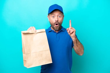 Orta yaşlı bir adam mavi arka planda izole edilmiş bir paket yiyecek alıyor. Çözümü bulmak için parmağını kaldırıyor.