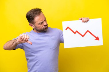 Orta yaşlı, sarı arka planda izole edilmiş beyaz bir adam elinde azalan bir istatistik ok sembolü olan ve kötü sinyal veren bir tabela tutuyor.