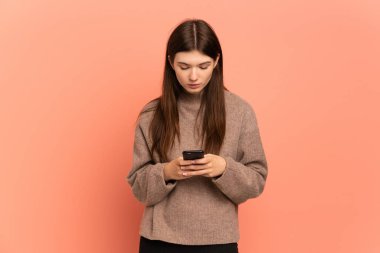 Genç Ukraynalı kız cep telefonu kullanarak pembe arka planda izole edilmiş.