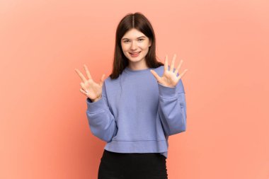 Pembe arka planda izole edilmiş genç Ukraynalı kız parmaklarıyla sekiz sayıyor.