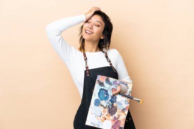 Genç bir sanatçı arka planda palet tutuyor ve gülüyor.