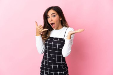 Pembe arka planda izole edilmiş genç beyaz bir kadın telefon jesti yapıyor.