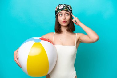 Plaj topu tutan genç Ukraynalı kadın mavi arka planda izole edilmiş şüpheleri ve düşünceleri var.