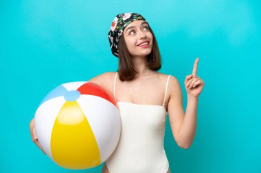 Elinde plaj topu tutan genç Ukraynalı bir kadın mavi arka planda izole edilmiş harika bir fikre işaret ediyor.