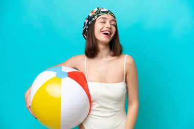 Young Ukrainian woman holding beach ball isolated on blue background laughing
