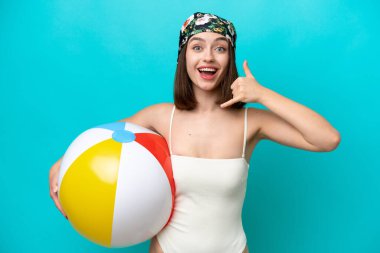 Elinde plaj topu tutan genç Ukraynalı bir kadın mavi arka planda izole bir şekilde telefon jesti yapıyor. Bana geri dönüş işareti ver.