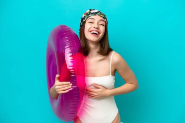 Mavi arka planda şişme yatak tutan genç Ukraynalı kadın çok gülümsüyor.