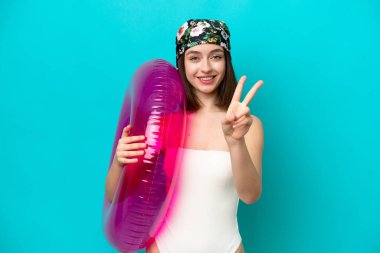 Mavi arka planda hava yatağı tutan genç Ukraynalı kadın gülümsüyor ve zafer işareti gösteriyor.