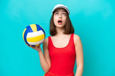 Genç Ukraynalı bir kadın, plajda voleybol oynuyor mavi arka planda izole bir şekilde yukarı bakıyor ve şaşırmış bir ifadeyle