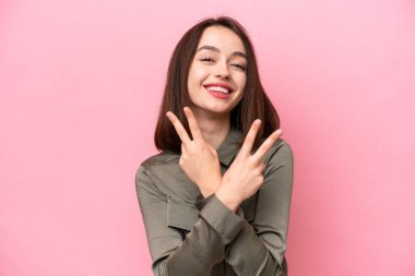 Pembe arka planda izole edilmiş genç Ukraynalı kadın gülümsüyor ve zafer işareti gösteriyor.