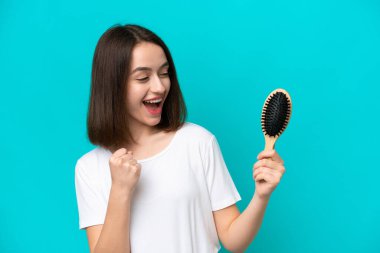 Mavi arka planda saç tarağı olan genç Ukraynalı kadın zaferi kutluyor.