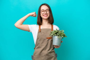 Bahçıvan Ukraynalı kadın elinde mavi arka planda izole edilmiş bir bitki tutuyor güçlü bir jest yapıyor