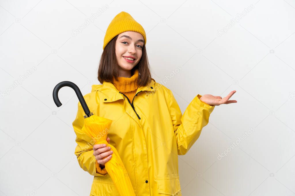 Young Ukrainian woman with rainproof coat and umbrella isolated on white background extending hands to the side for inviting to come