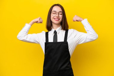 Sarı arka planda izole edilmiş genç Ukraynalı garson kadın güçlü bir jest yapıyor.