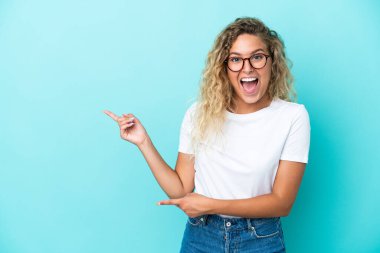 Mavi arka planda yalnız, kıvırcık saçlı kız şaşırmış ve işaret ediyor.