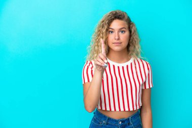 Kıvırcık saçlı kız mavi arka planda izole edilmiş, ciddi bir ifadeye sahip birini sayıyor.