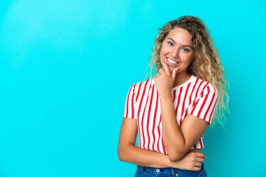 Mavi arka planda yalnız, kıvırcık saçlı mutlu ve gülümseyen bir kız.