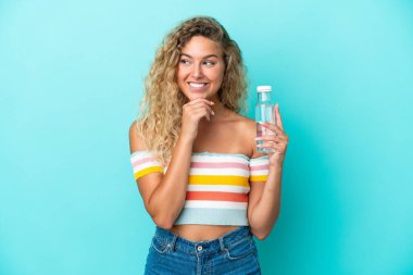 Mavi arka planda bir şişe suyu olan genç sarışın kadın yan tarafa bakıyor ve gülümsüyor.