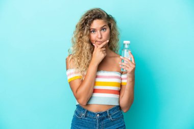Mavi arka planda bir şişe suyla izole edilmiş genç sarışın kadın