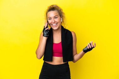 Sarı arka planda izole edilmiş havlusu olan sporcu bir kadın cep telefonuyla sohbet ediyor.