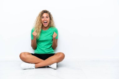 Kıvırcık saçlı kız yerde oturmuş zaferi kutluyor.