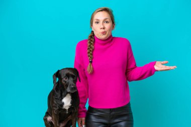 Mavi arka planda köpeği olan beyaz bir kadın omuzlarını kaldırırken şüpheyle hareket ediyor.