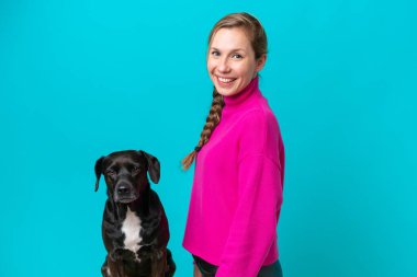 Köpeği olan beyaz bir kadın mavi arka planda izole edilmiş ve gülümsüyor.