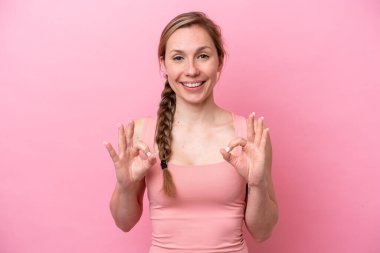 Pembe arka planda izole edilmiş beyaz bir kadın iki eliyle tamam işareti gösteriyor.
