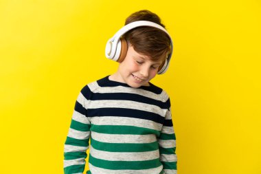 Sarı arka planda izole edilmiş küçük kızıl çocuk müzik dinliyor.