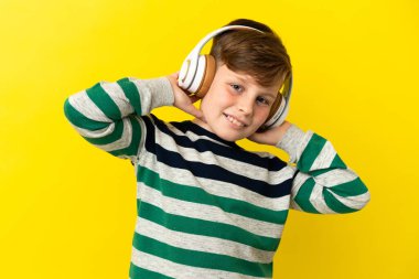 Sarı arka planda izole edilmiş küçük kızıl çocuk müzik dinliyor.