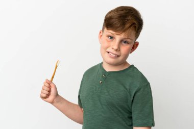 Beyaz arka planda izole edilmiş diş fırçası tutan kızıl saçlı çocuk çok gülümsüyor.