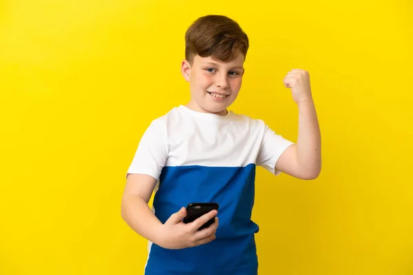 Kis Vörös Hajú Fiú Elszigetelt Sárga Háttér Telefon Győzelmi Pozícióban — Stock Fotó