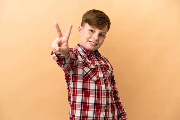 Pequeno Menino Ruivo Isolado Fundo Bege Sorrindo Mostrando Sinal Vitória — Fotografia de Stock