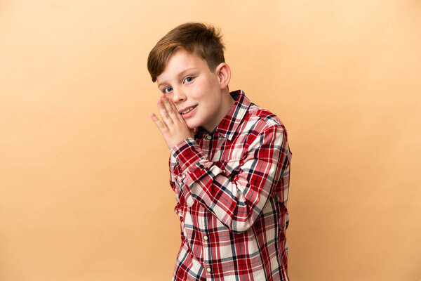 Little redhead boy isolated on beige background whispering something