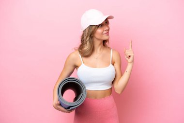 Genç sporcu kadın yoga derslerine giderken elinde minder tutarak harika bir fikri işaret ediyor.