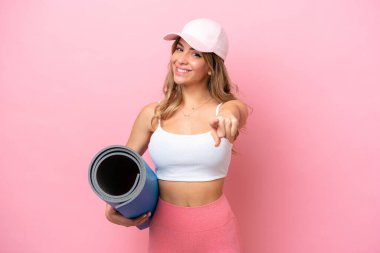 Genç sporcu kadın yoga derslerine giderken elinde mutlu bir ifadeyle önü gösteren bir minder tutuyor.