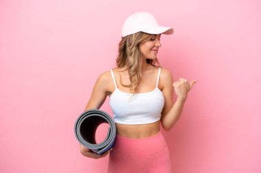 Genç sporcu kadın yoga derslerine giderken elinde bir hasırla ürünü sunuyor.