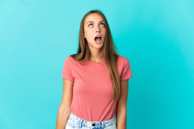 Soyutlanmış mavi arka planda genç bir kadın yukarı bakıyor ve şaşırmış bir ifadeyle