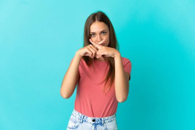 İzole edilmiş mavi arka planda genç bir kadın sessizlik işareti gösteriyor.