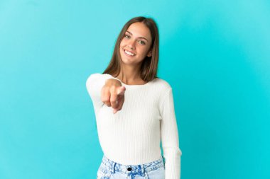 Soyutlanmış mavi arka planda genç bir kadın mutlu bir ifadeyle öne bakıyor.