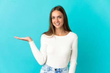 İzole edilmiş mavi arka plan üzerinde genç bir kadın bir ilan vermek için avucunun içinde hayali bir alan tutuyor.