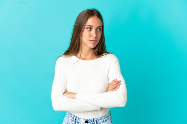 İzole edilmiş mavi arka planı olan genç bir kadın kollarını çapraz tutuyor.