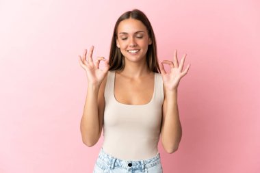 Zen pozisyonunda soyutlanmış pembe arka planı olan genç bir kadın.