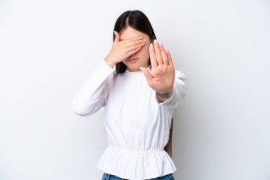 Beyaz arka planda izole edilmiş genç Çinli kadın dur hareketi yapıyor ve yüzünü kapatıyor.