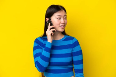 Sarı arka planda izole edilmiş genç Çinli bir kadın cep telefonuyla sohbet ediyor.