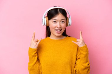 Genç Çinli bir kadın pembe arka planda izole edilmiş rock hareketlerini dinliyordu.