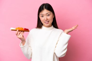 Pembe arka planda saşimi tutan genç Çinli kadın davet edilmek için ellerini yana uzatıyor.