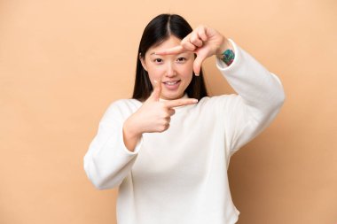 Yüzüne odaklanan bej arka planda izole edilmiş genç bir Çinli kadın. Çerçeve sembolü